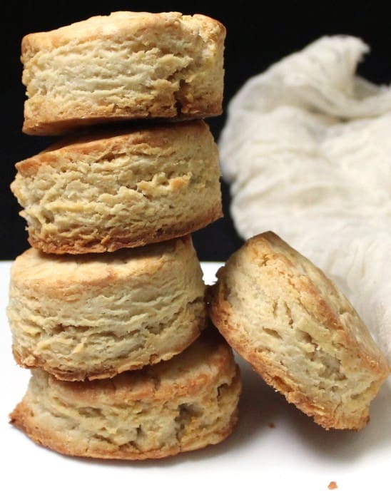 Four vegan sourdough biscuits stacked on top of each other with one leaning against them and a white cheesecloth in background