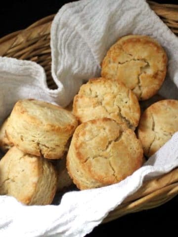 Close up shot of vegan sourdough biscuits nestled in a wicker basket with a flour sack napkin