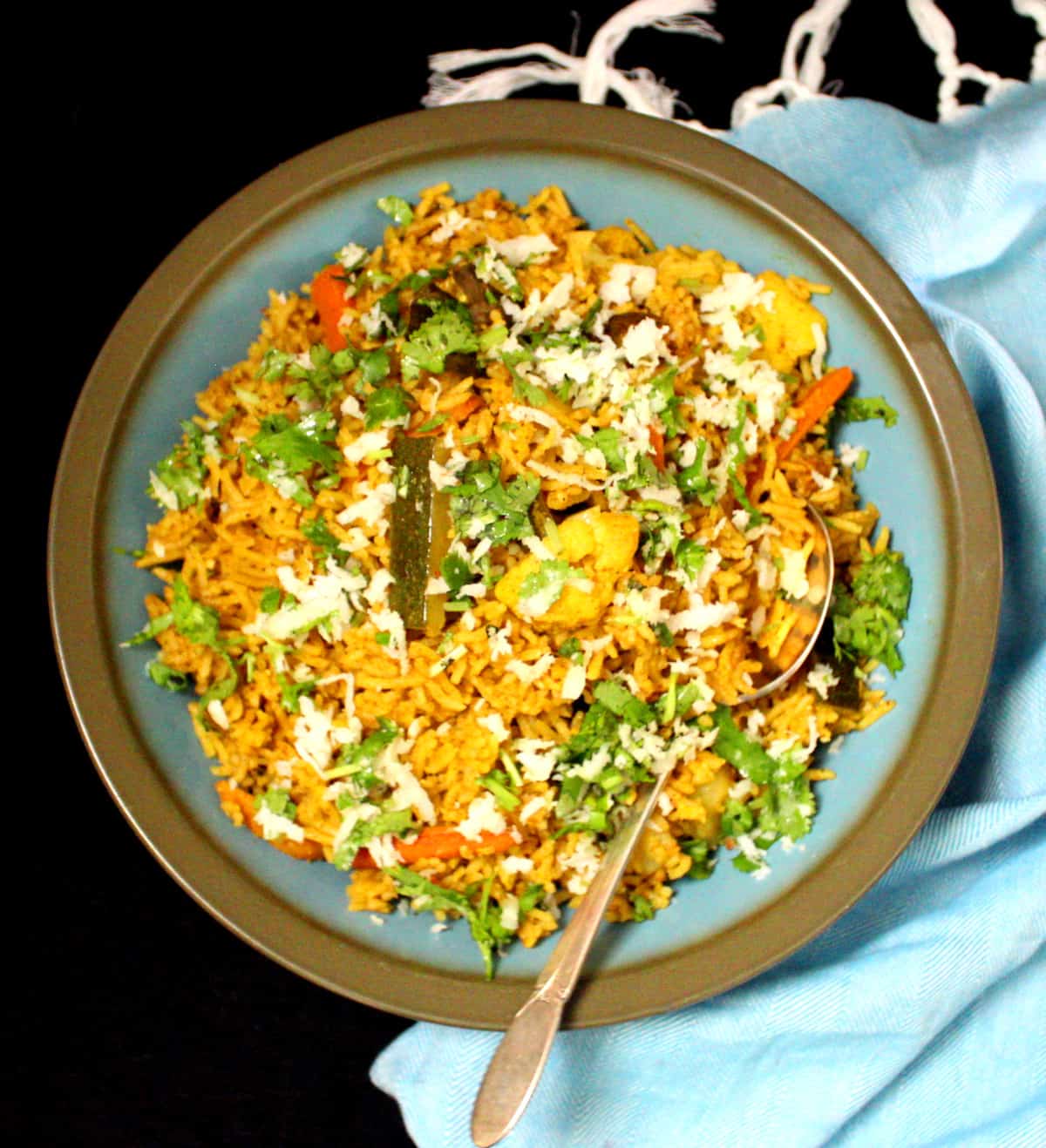 Spicy masale bhath in a blue and brown bowl with a spoon and blue napkin.