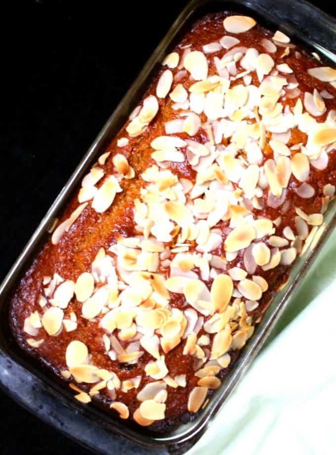A top close up shot of a bright orange vegan mango bread strewn with blanched, sliced almonds in a loaf pan.