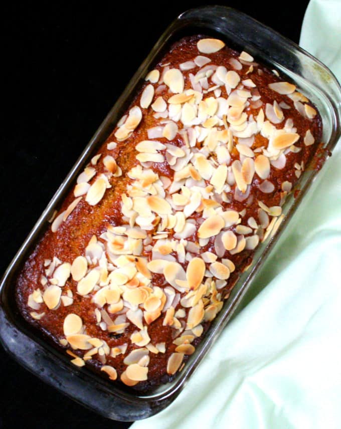 Vegan mango bread with blanched almonds in glass loaf pan.