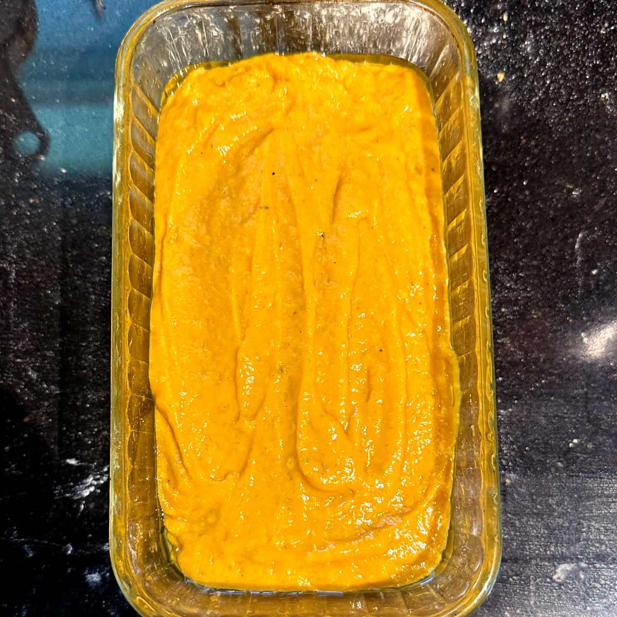 Mango bread batter in glass loaf pan before baking.