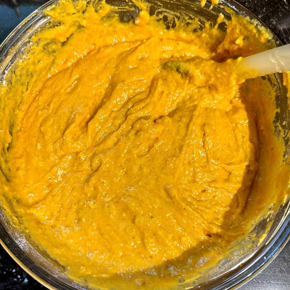 Vegan mango bread batter mixed with spatula in bowl.