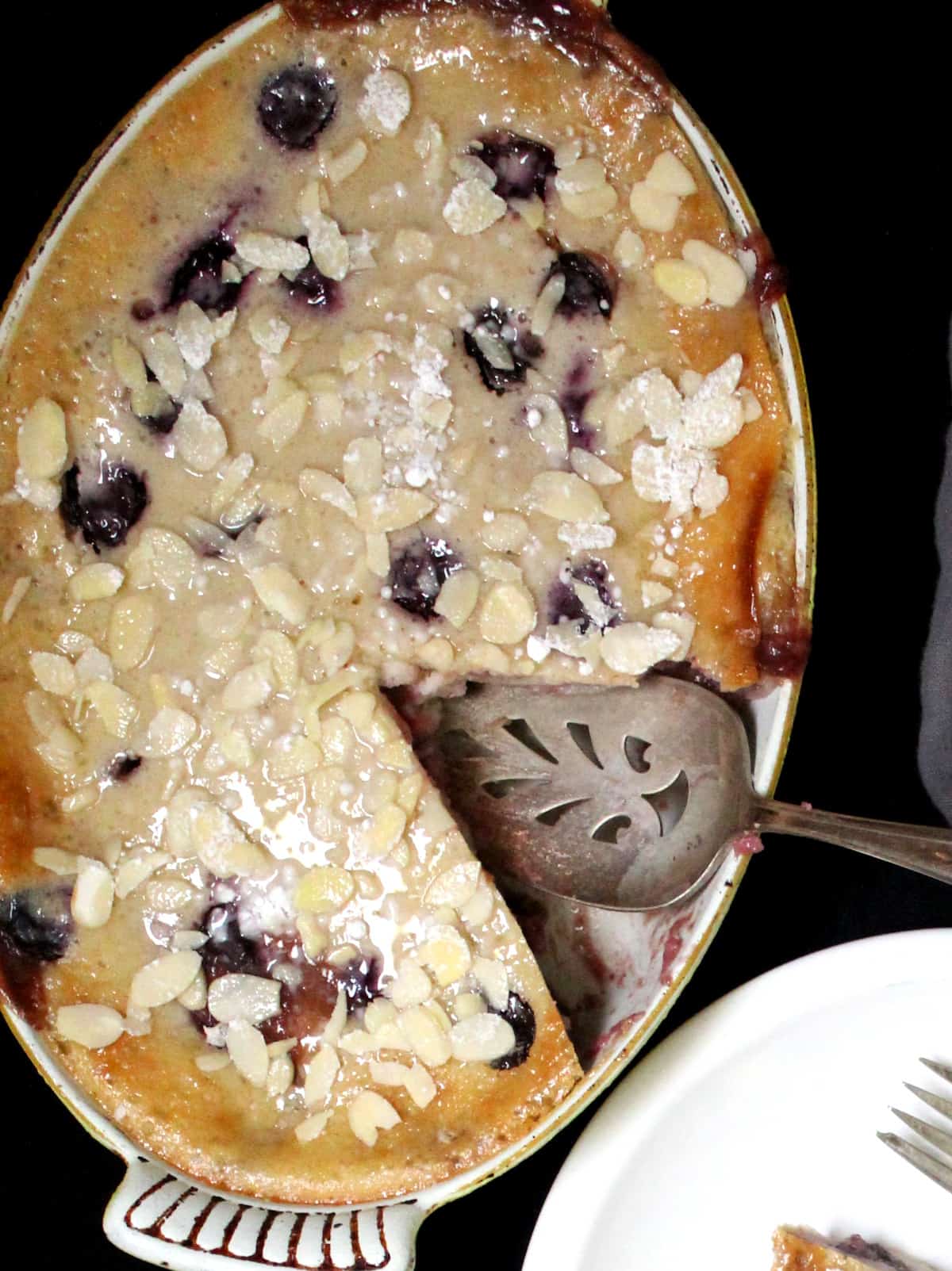 Vegan Cherry Clafoutis in an oval ceramic baking dish with a decorative pie server