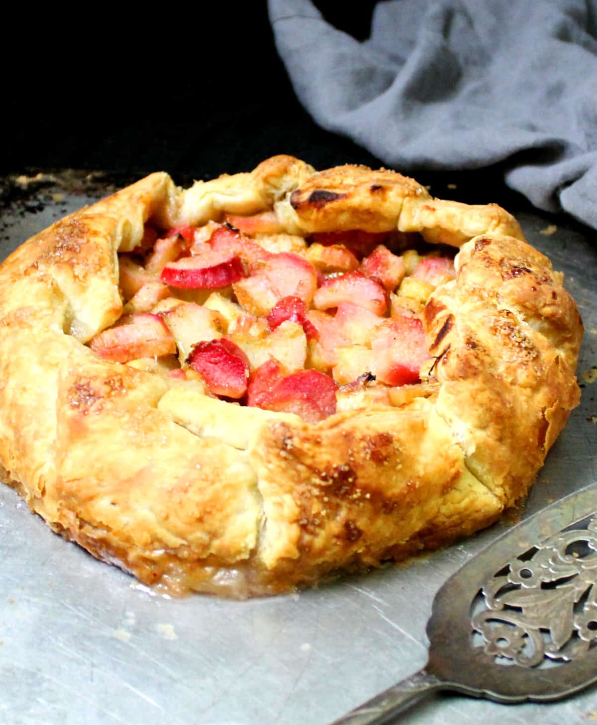 Front short of a rhubarb galette with a pie server and a gray napkin.
