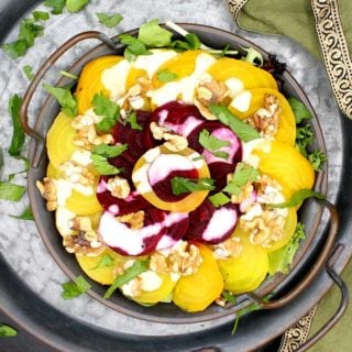 Closeup shot of a tray with a serving plate of golden and red beets arranged in a decorative pattern with walnuts, fancy greens and creamy dressing and parsley