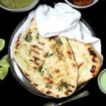 A stack of vegan grilled naans in a silver plate with chutney, lemons, dal and a spicy Indian curry