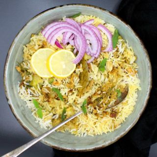Overhead shot of a bowl of keema biryani, an Indian rice dish with ground meatless meat and spices, in a glazed bowl with a spoon, lemons and sliced onions