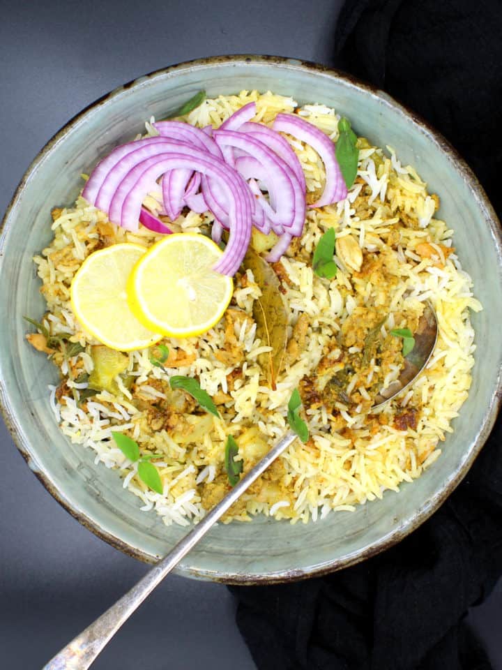 A bowl of keema biryani with onions and slices of lemon and a spoon.