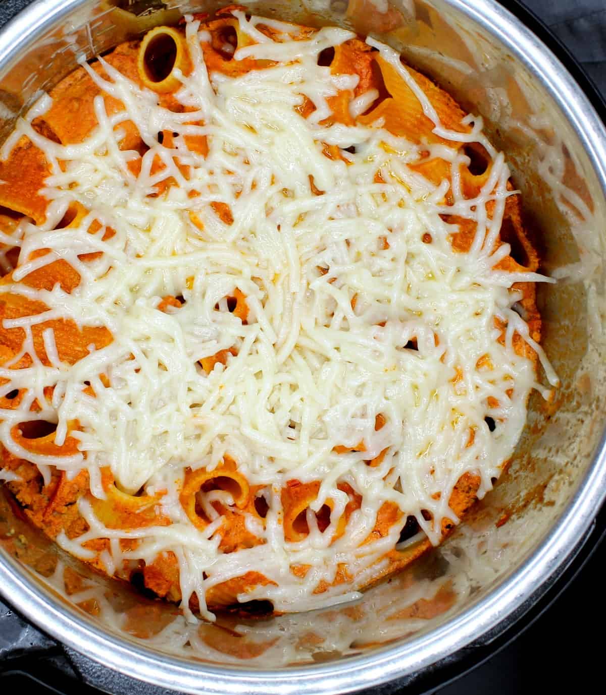 An overhead shot of an Instant Pot liner with freshly baked creamy, cheesy vegan pasta bake with rigatoni, shreds of vegan mozzarella cheese and a gray napkin.