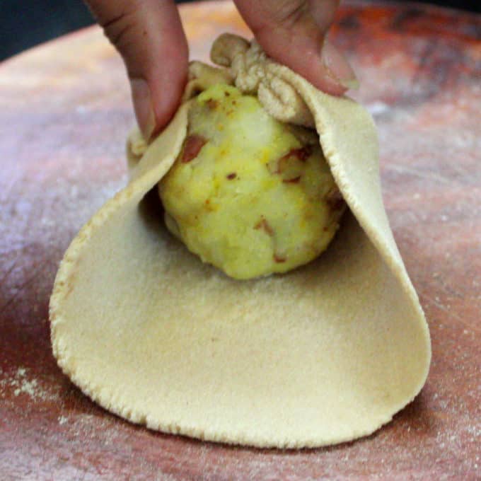 Folding the dough over the aloo paratha to form a ball