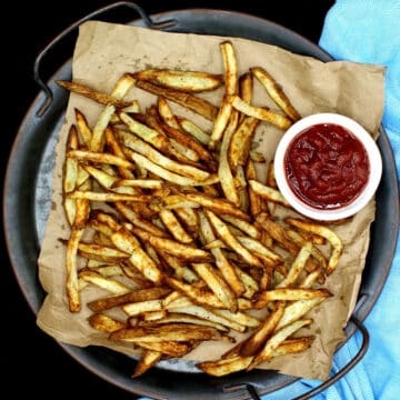 Air fryer French fries on brown paper in plate with a side of ketchup in bowl.