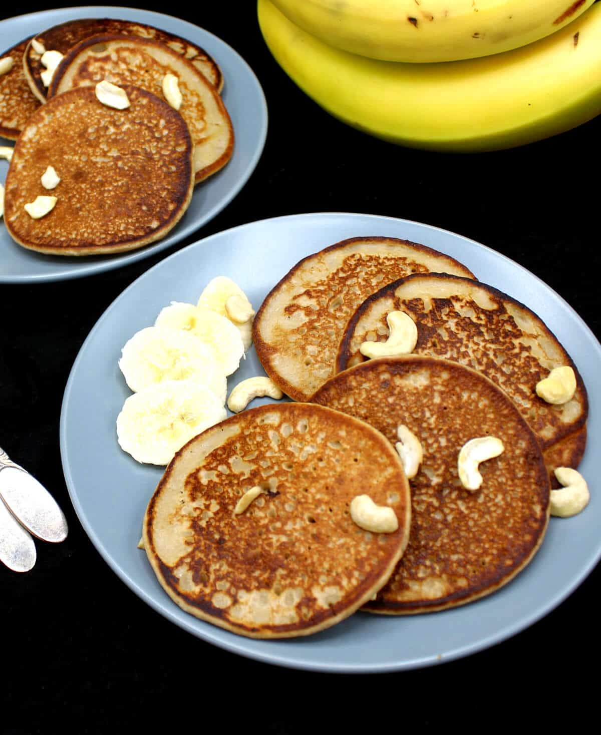 Banana dosas served with fresh slices of bananas on gray ceramic plates with bananas and forks in the background with a cheesecloth
