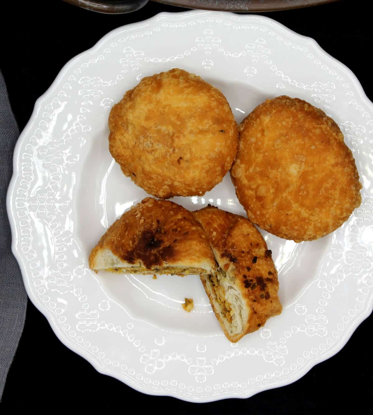 Two kachoris on a white plate with a stuffing of moong dal, besan, fennel and other spices.