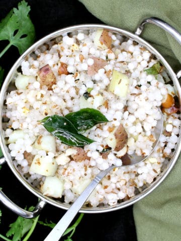 A steel wok with sabudana khichdi garnished with cilantro, curry leaves and peanuts with a green napkin