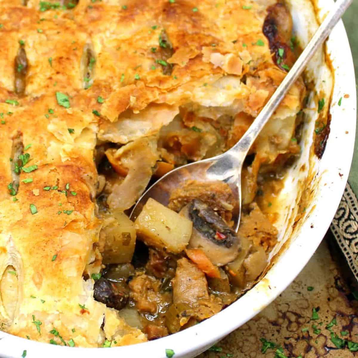 Vegan pot pie with crackly golden crust and a filling of chunky vegetables in a savory stew with spoon.