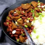 Vegan red beans and rice in a black bowl with a decorative spoon against a gray napkin