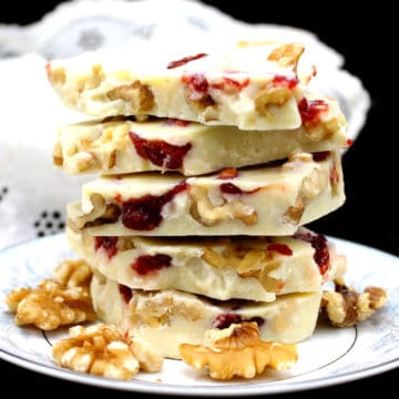A stack of vegan white chocolate bark or candy pieces with raspberry and walnuts in a white and blue porcelain plate