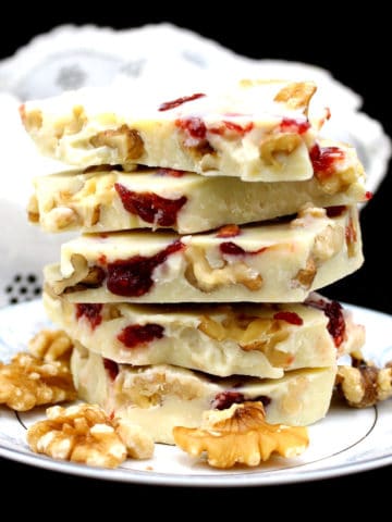 A stack of vegan white chocolate bark or candy pieces with raspberry and walnuts in a white and blue porcelain plate