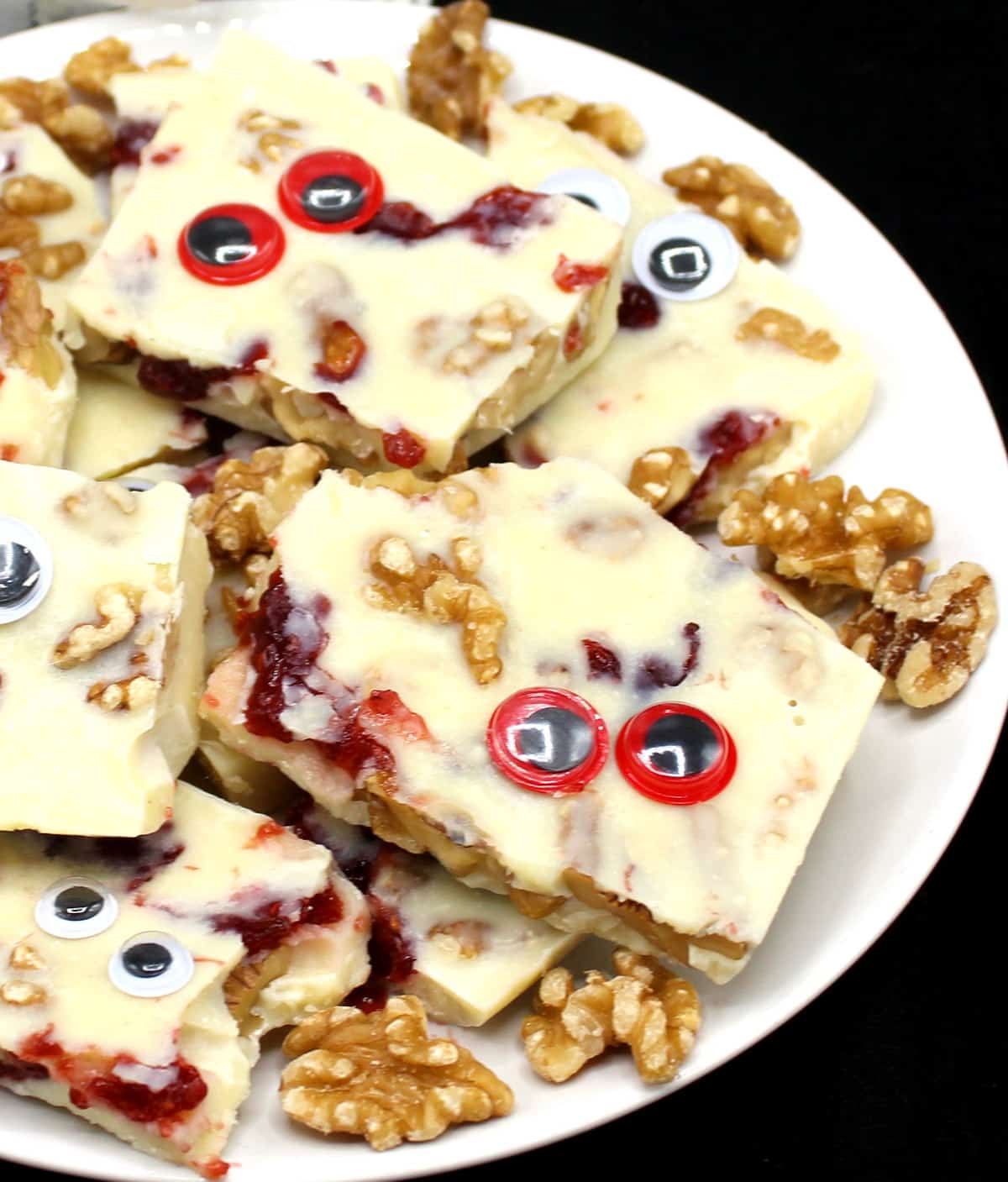 Vegan White Chocolate Bark with raspberry "blood" and smashed walnut "brains" and googly eyes in a white plate, for Halloween.