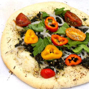 A colorful Manakish with spinach, za'atar. sweet peppers and cherry tomatoes on a white background