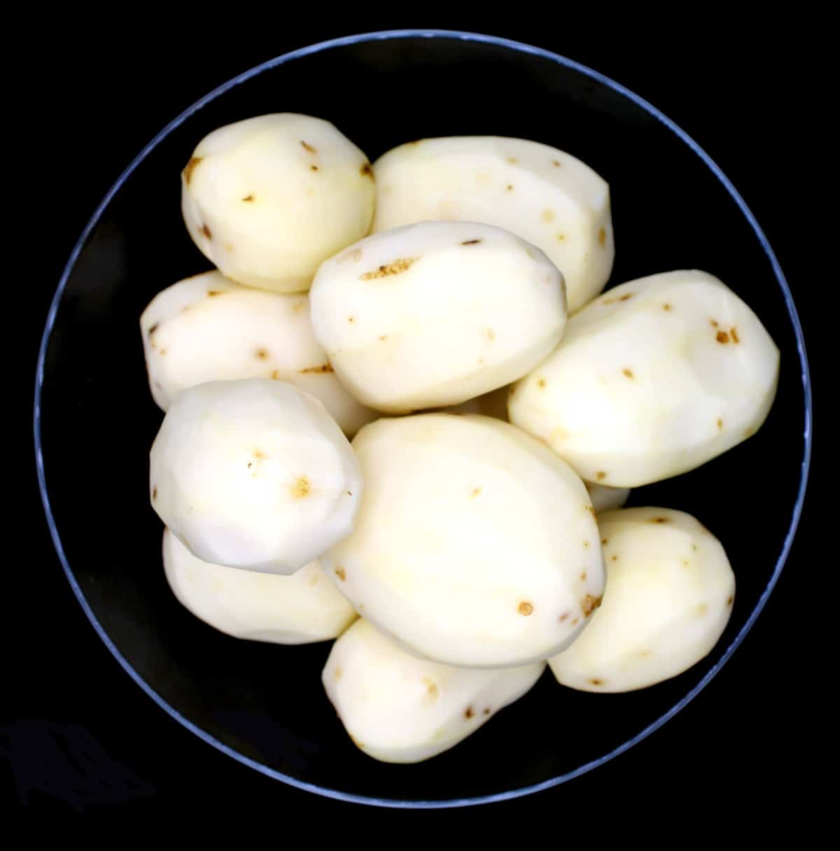 Peeled potatoes in black bowl.