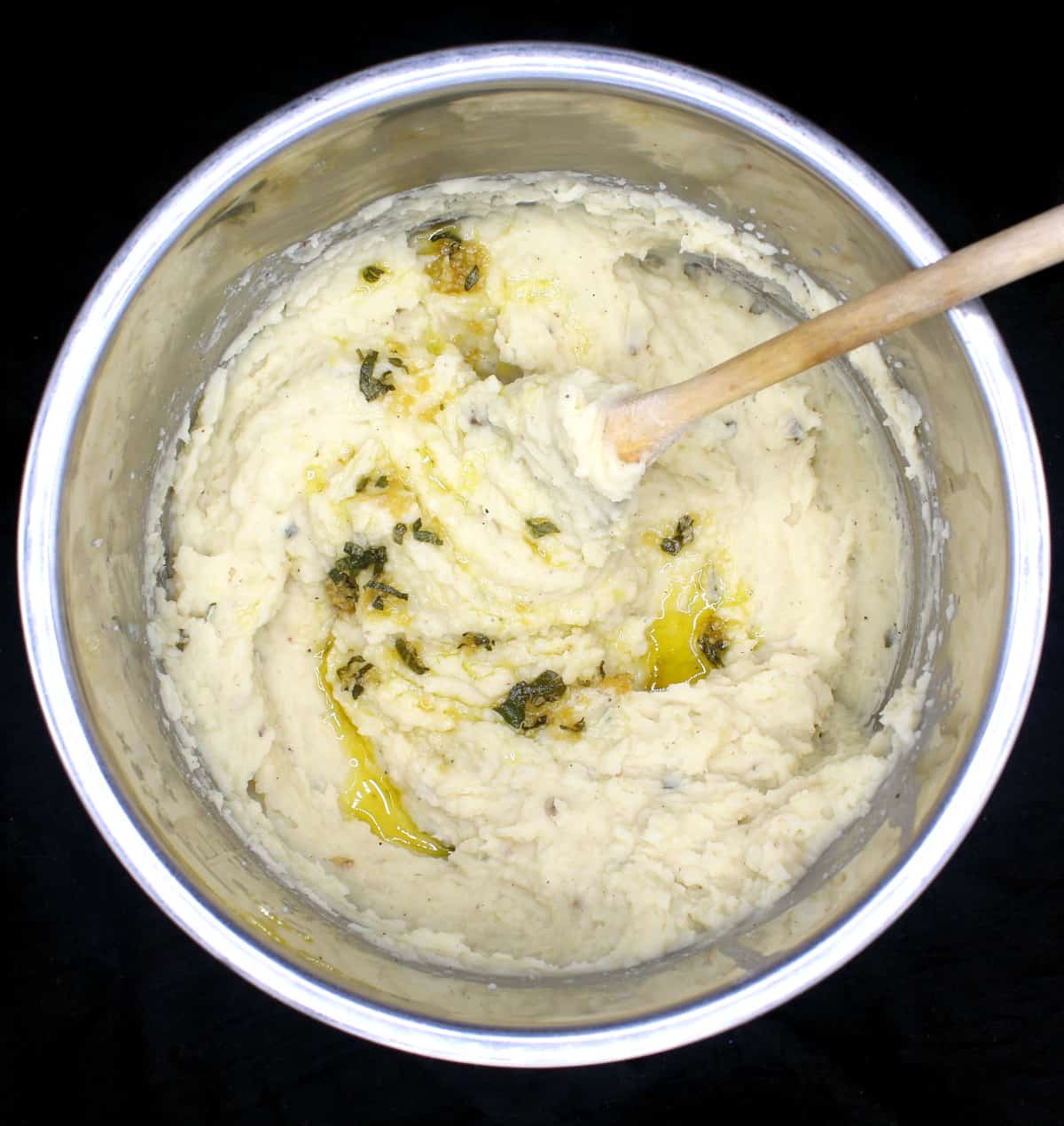 An Instant Pot liner with buttery mashed potatoes infused with sage and garlic olive oil with a ladle on a black background.