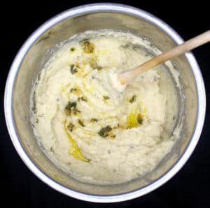 An overhead shot of Vegan Instant Pot Mashed Potatoes in a steel IP liner with sage garlic olive oil and a wooden ladle on a black background