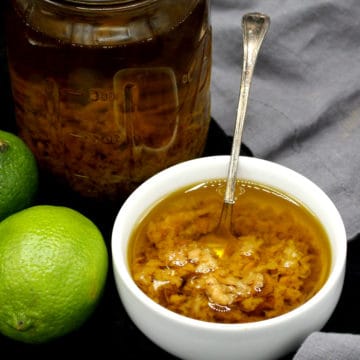 A bowl of mojo de ajo with a jar and limes in the background.