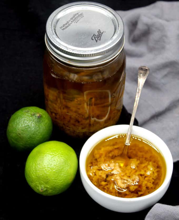 A bowl and a jar with mojo de ajo with whole limes on the side.