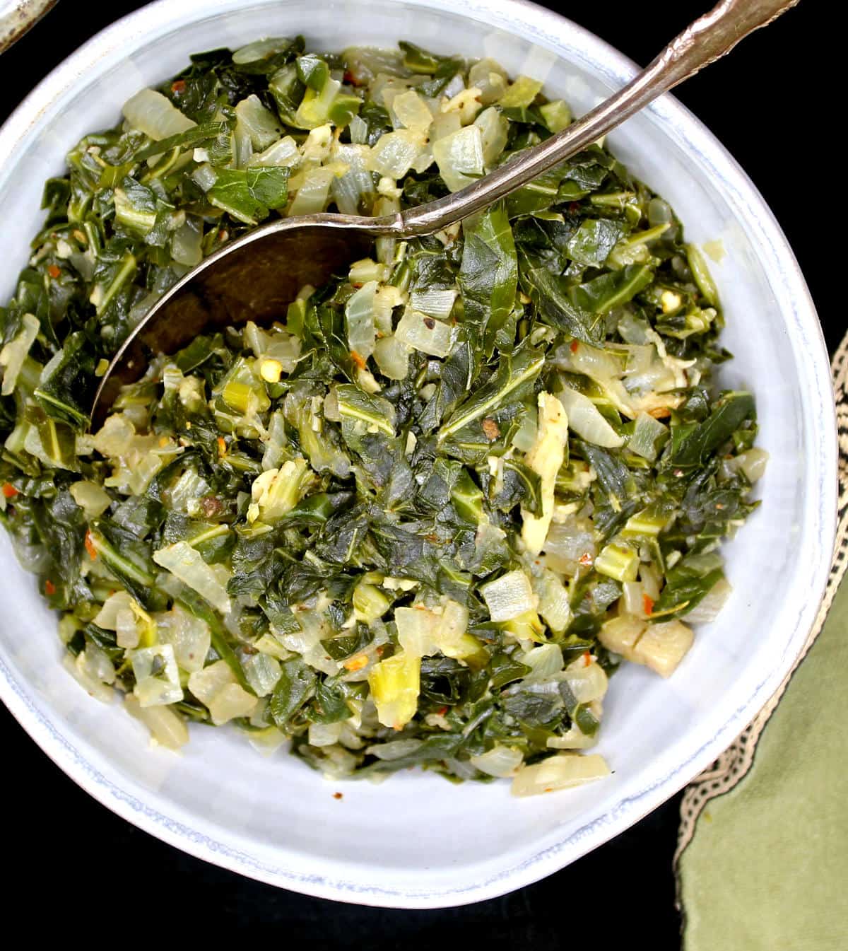 A closeup of braised southern style collard greens in a ceramic gray bowl with a silver spoon.