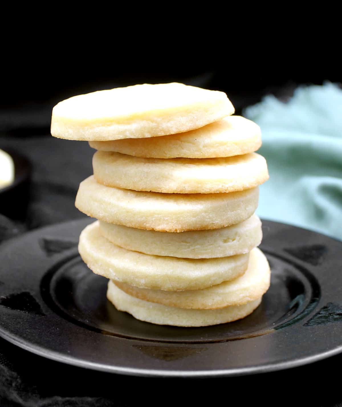 Round sugar cookies stacked on a black plate with a green napkin.