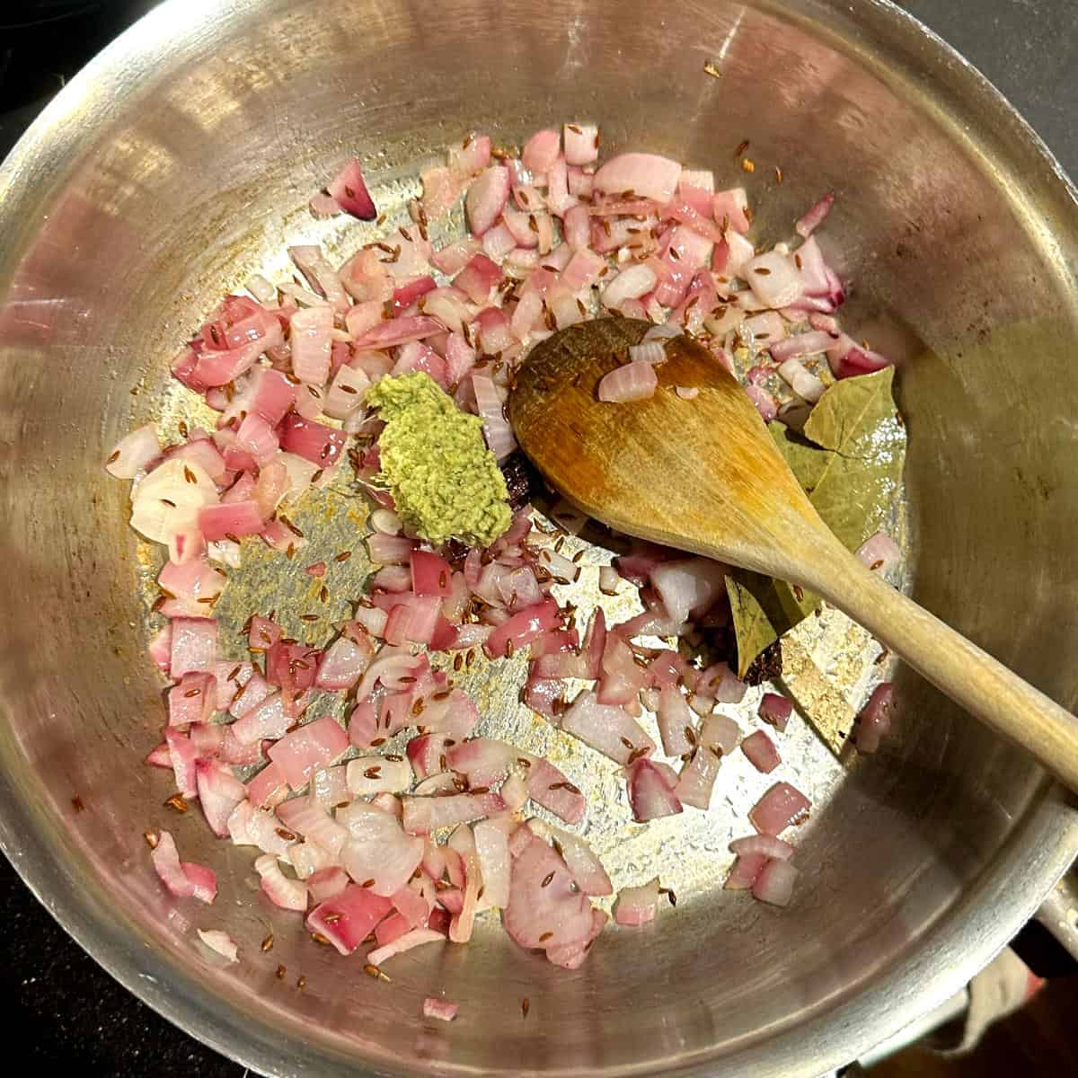 Photo of onions frying in pot with ginger garlic paste added.