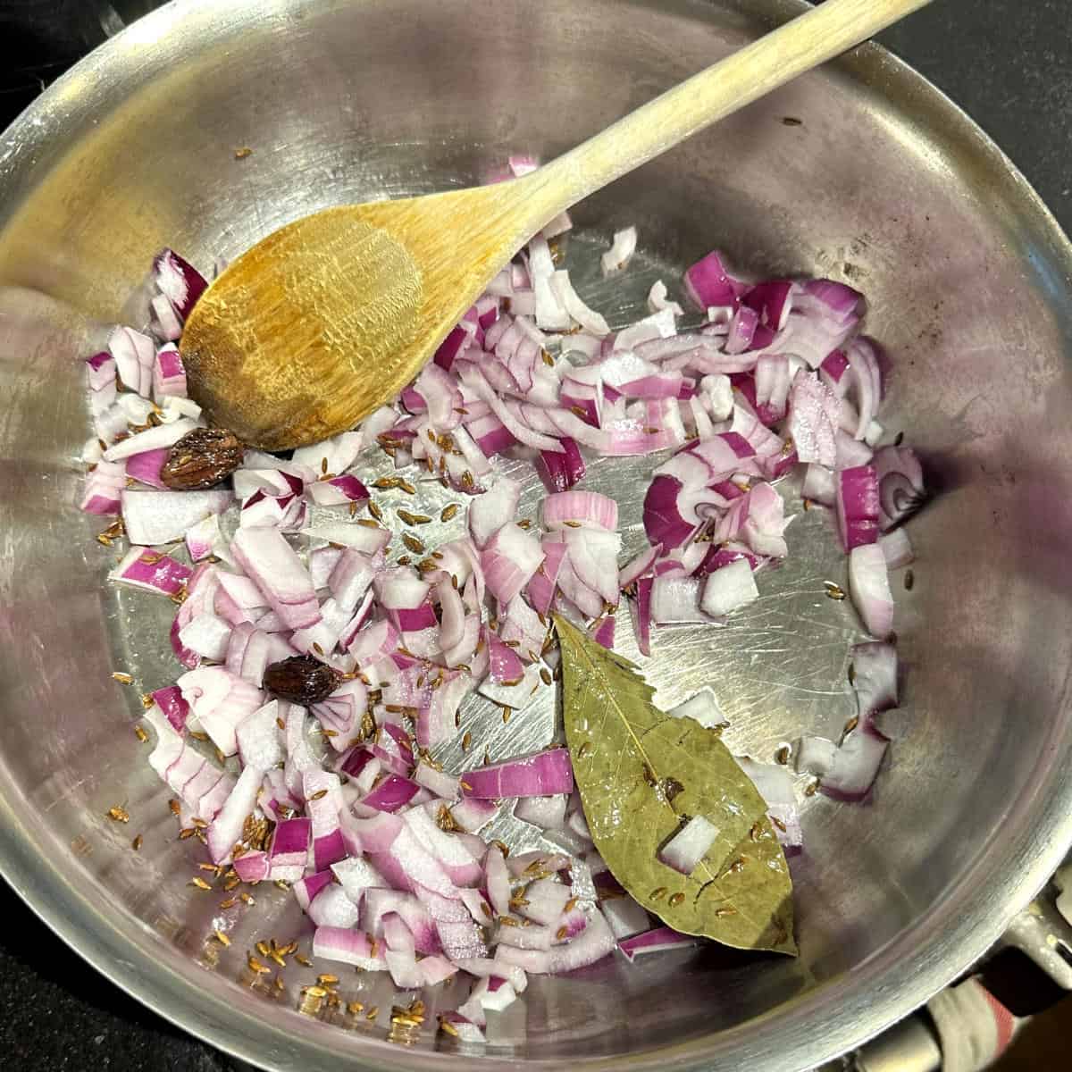 Photo of onions added to spices in pot.