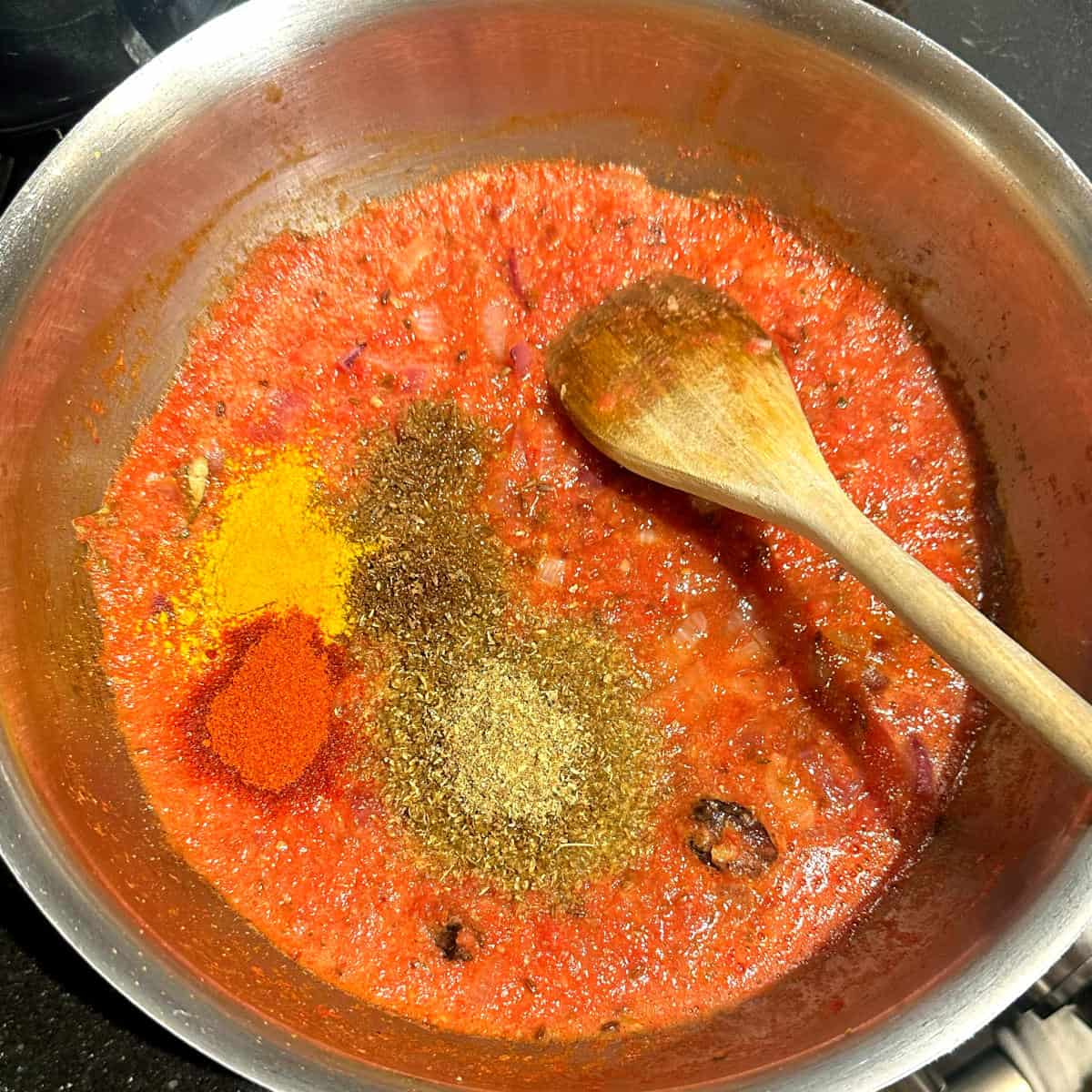 Spices added to tomatoes and onions in pot.