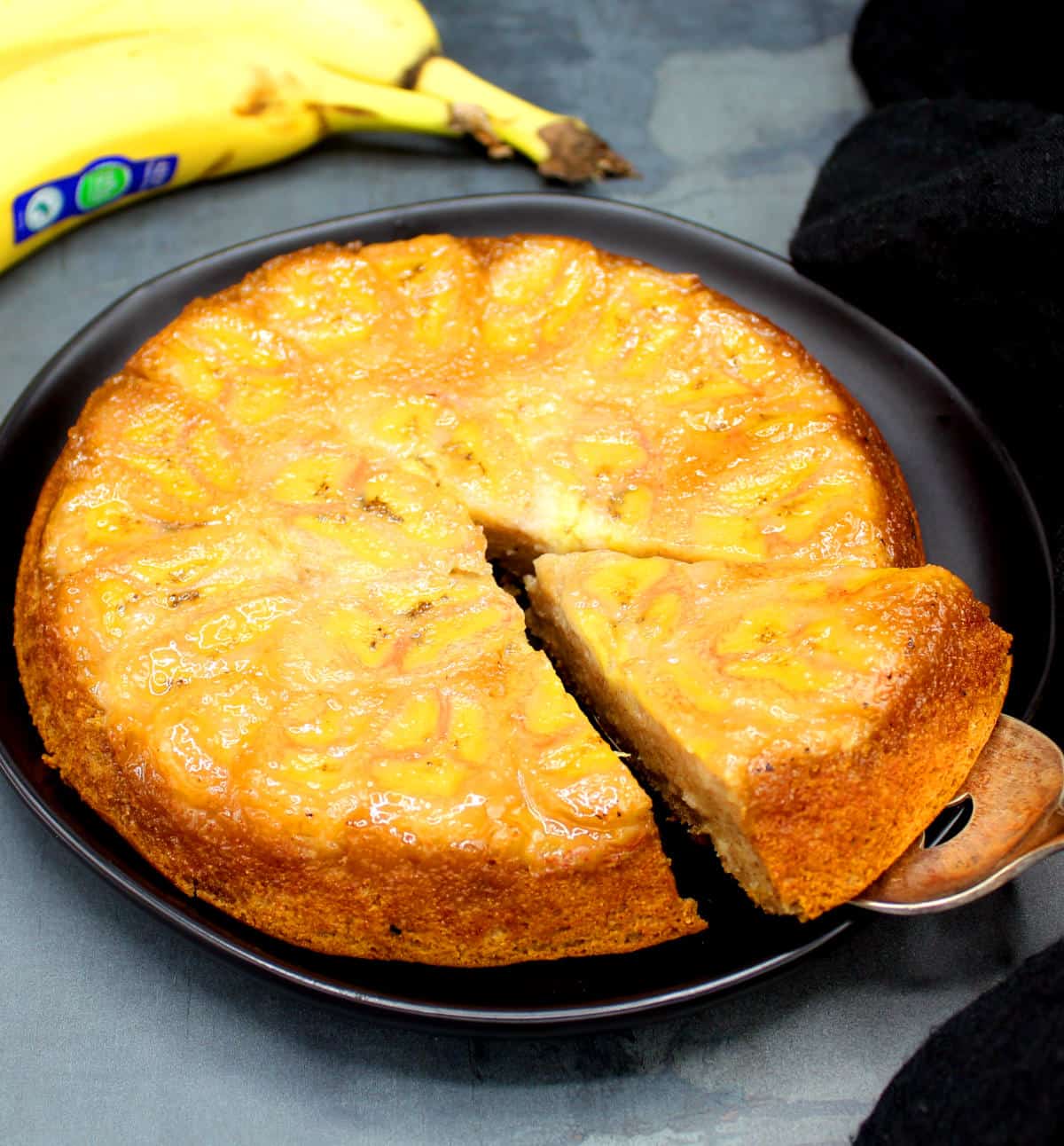 A slice of the banana upside down cake being lifted off with a serving spoon.