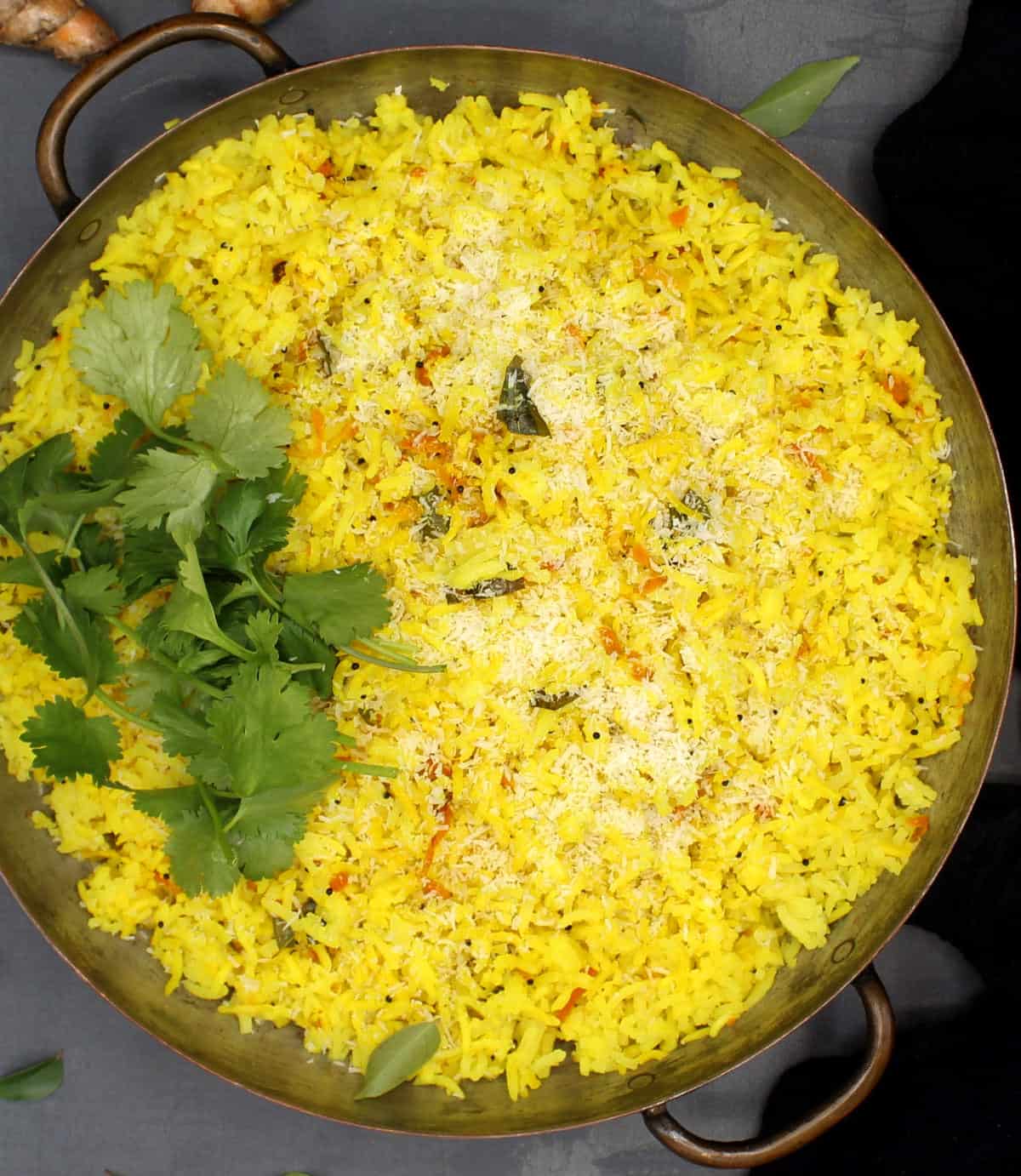 Yellow turrmeric rice with curry leaves, cilantro, coconut in a skillet on gray background.