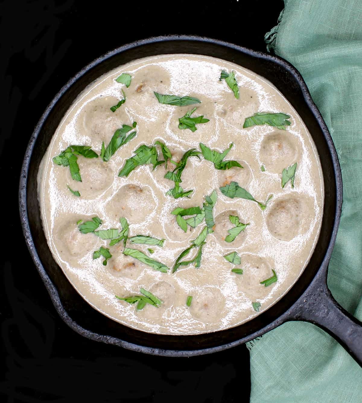 A cast iron skillet with vegan air fryer meatballs in a creamy mushroom sauce garnished with parsley.