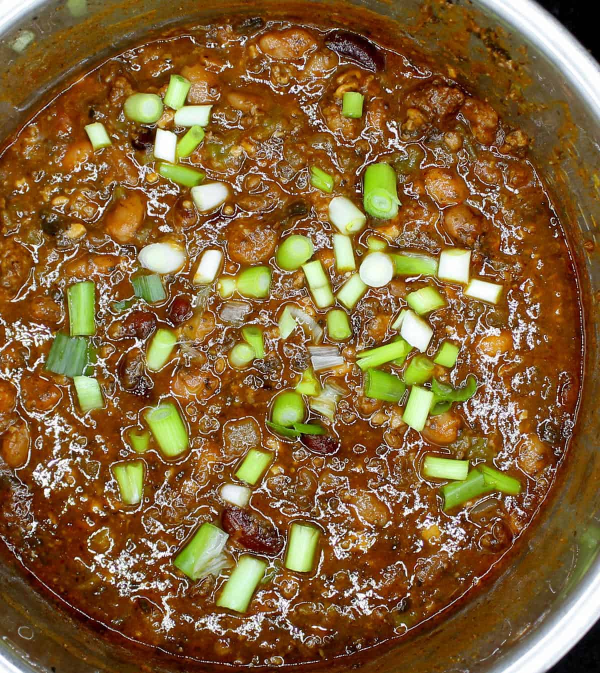A closeup of cooked vegan chili in an Instant Pot steel liner with scallions.