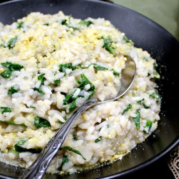 A closeup shot of a black ceramic bowl with creamy vegan risotto with spinach