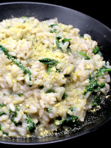 A closeup shot of a black ceramic bowl with creamy vegan risotto with spinach