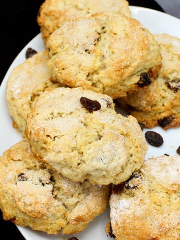 A stack of fluffy vegan currant scones in a white plate with black currants or raisins
