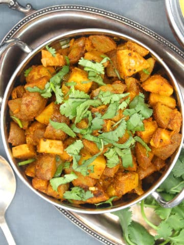 Bombay Potatoes with tomatoes, shallots, curry powder, tomato and cilantro in a small Indian steel wok with cilantro and dal