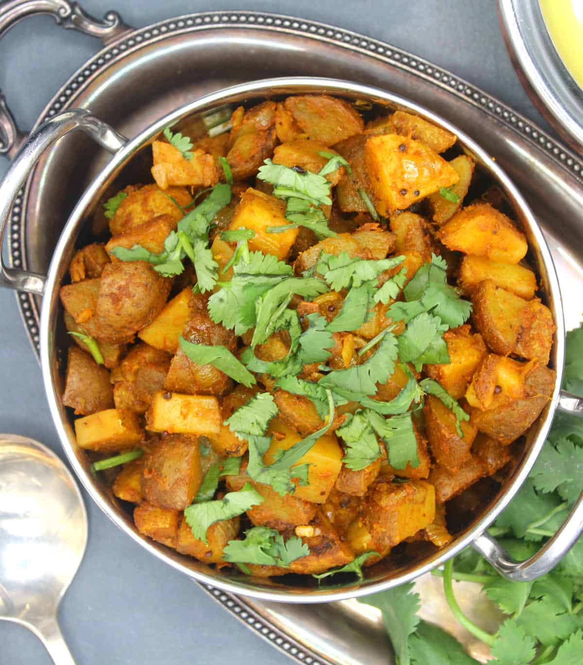 Bombay potatoes sauteed with shallots and tomatoes and curry spices in a steel kadhai with cilantro.