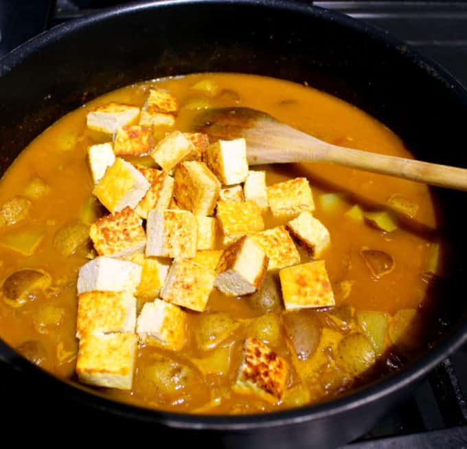 Tofu added to curry in saucepan.