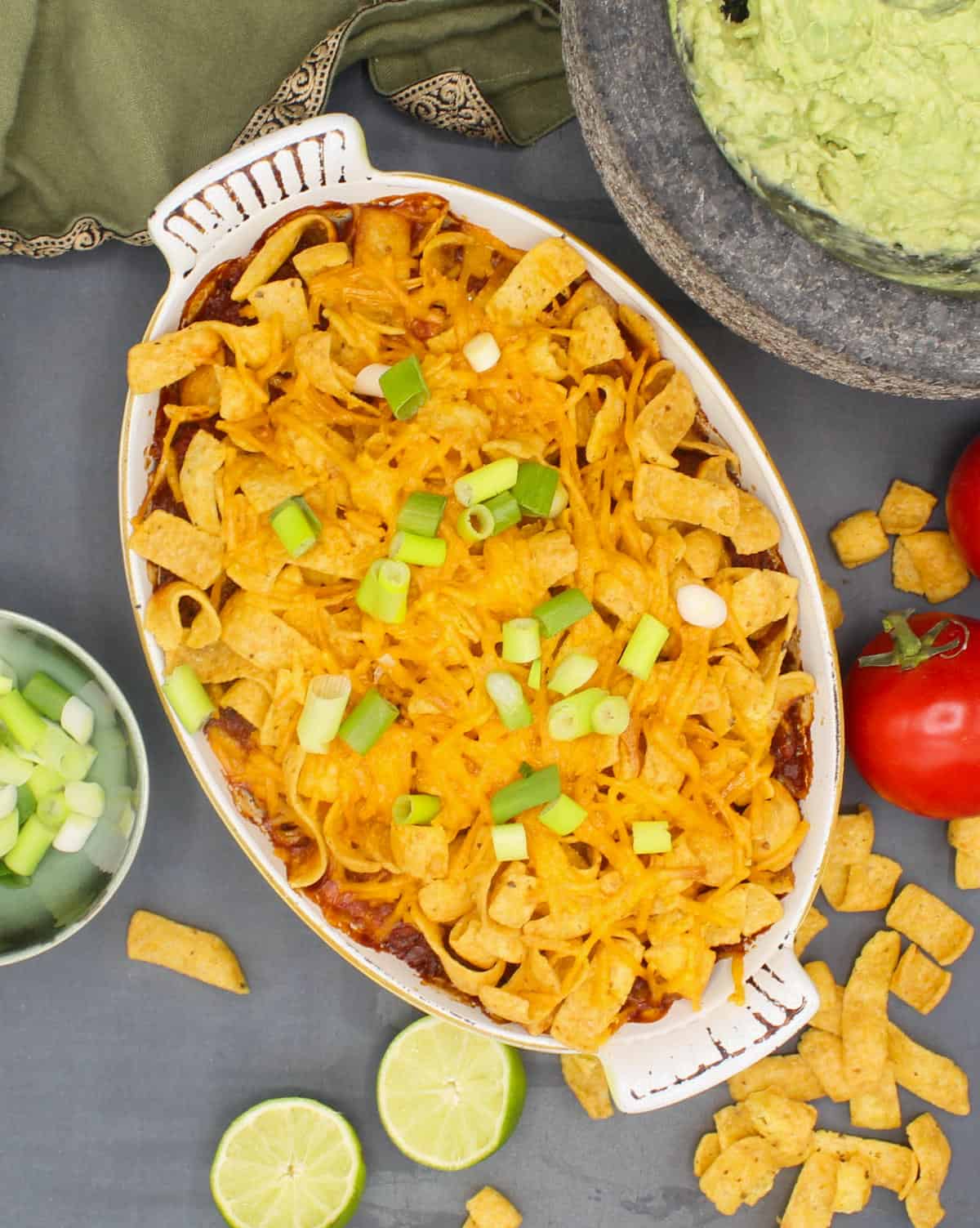Vegan Frito pie in baking dish with scallions, tomatoes and guacamole.