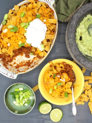 Vegan frito pie in baking dish and bowl with guacamole and scallions