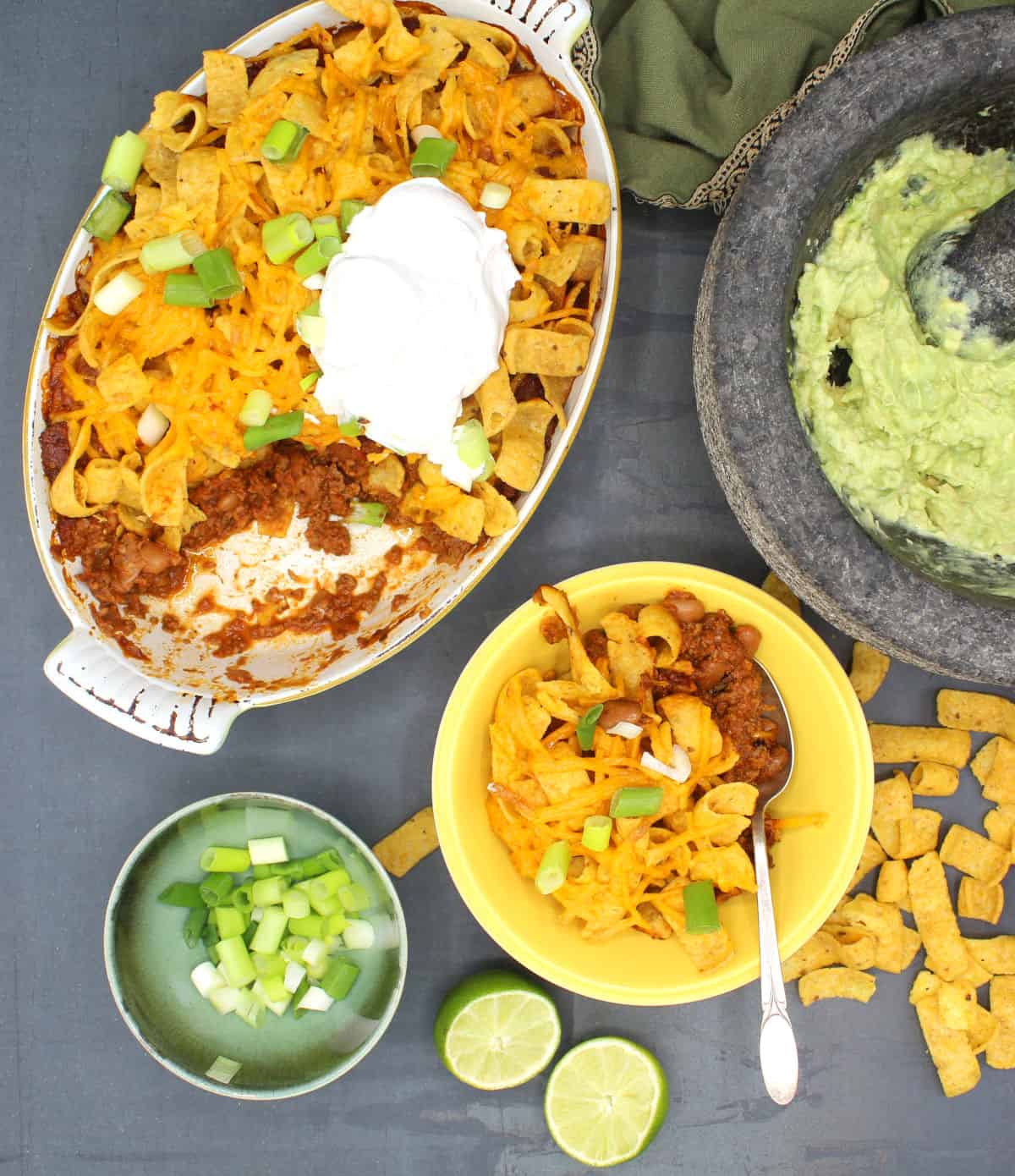 Vegan Frito pie in baking dish and bowl with vegan sour cream, scallions and guacamole.