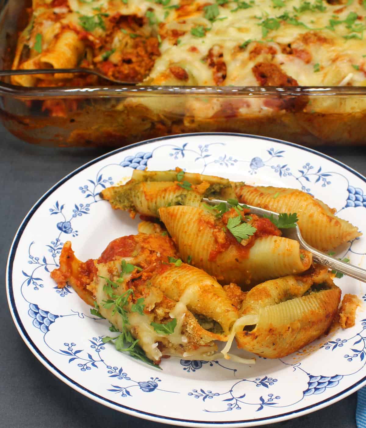 Stuffed pasta shells with spinach ricotta stuffing, marinara and parsley in an Italian blue and white dish with baking dish in the back.
