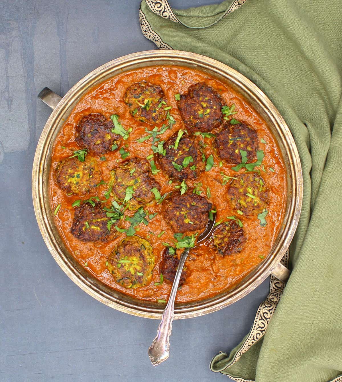 Zucchini kofta curry in a silver serving bowl with cilantro garnish.